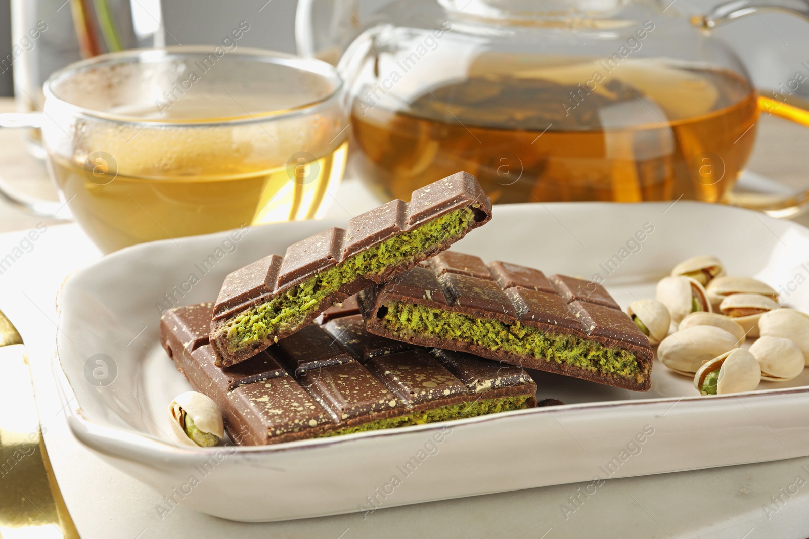 Pieces of delicious Dubai chocolate with pistachios, knafeh and tea on table, closeup Photo of Pieces of delicious Dubai chocolate with pistachios, knafeh and tea on table, closeup