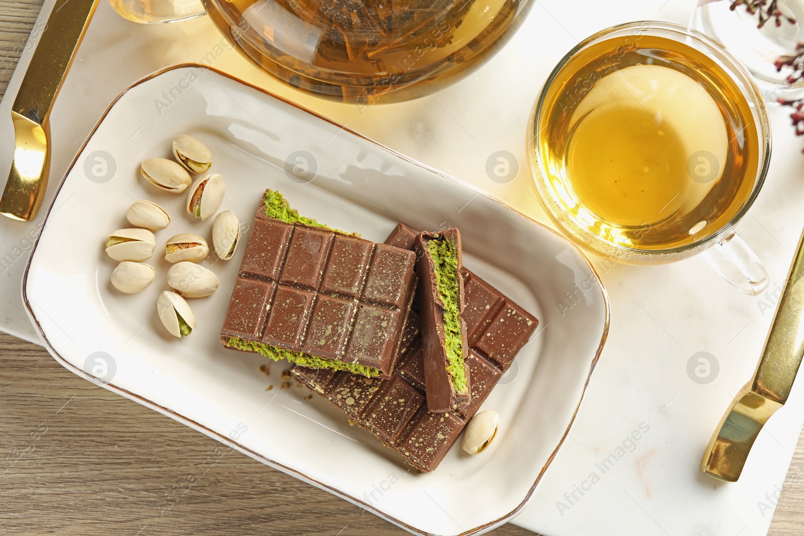 Photo of Pieces of delicious Dubai chocolate with pistachios, knafeh and tea on wooden table, flat lay