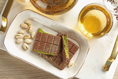 Photo of Pieces of delicious Dubai chocolate with pistachios, knafeh and tea on wooden table, flat lay