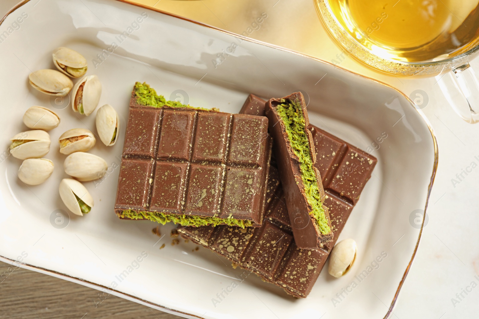 Pieces of delicious Dubai chocolate with pistachios, knafeh and tea on table, flat lay Photo of Pieces of delicious Dubai chocolate with pistachios, knafeh and tea on table, flat lay