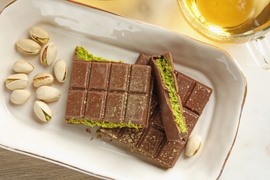 Photo of Pieces of delicious Dubai chocolate with pistachios, knafeh and tea on table, flat lay