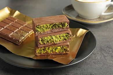 Photo of Pieces of delicious Dubai chocolate with pistachios and knafeh on grey table, closeup