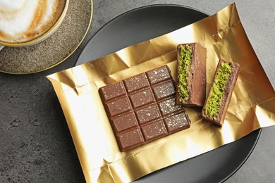 Photo of Pieces of delicious Dubai chocolate with pistachios, knafeh and coffee on grey table, flat lay