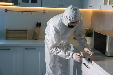 Photo of Forensic expert taking fingerprints from countertop with brush at crime scene indoors, space for text