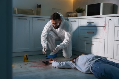 Photo of Forensic expert taking fingerprints with brush from gun and dead body at crime scene indoors