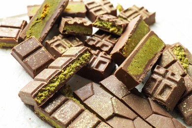 Photo of Pieces of tasty Dubai chocolate with pistachios and knafeh on white table, closeup