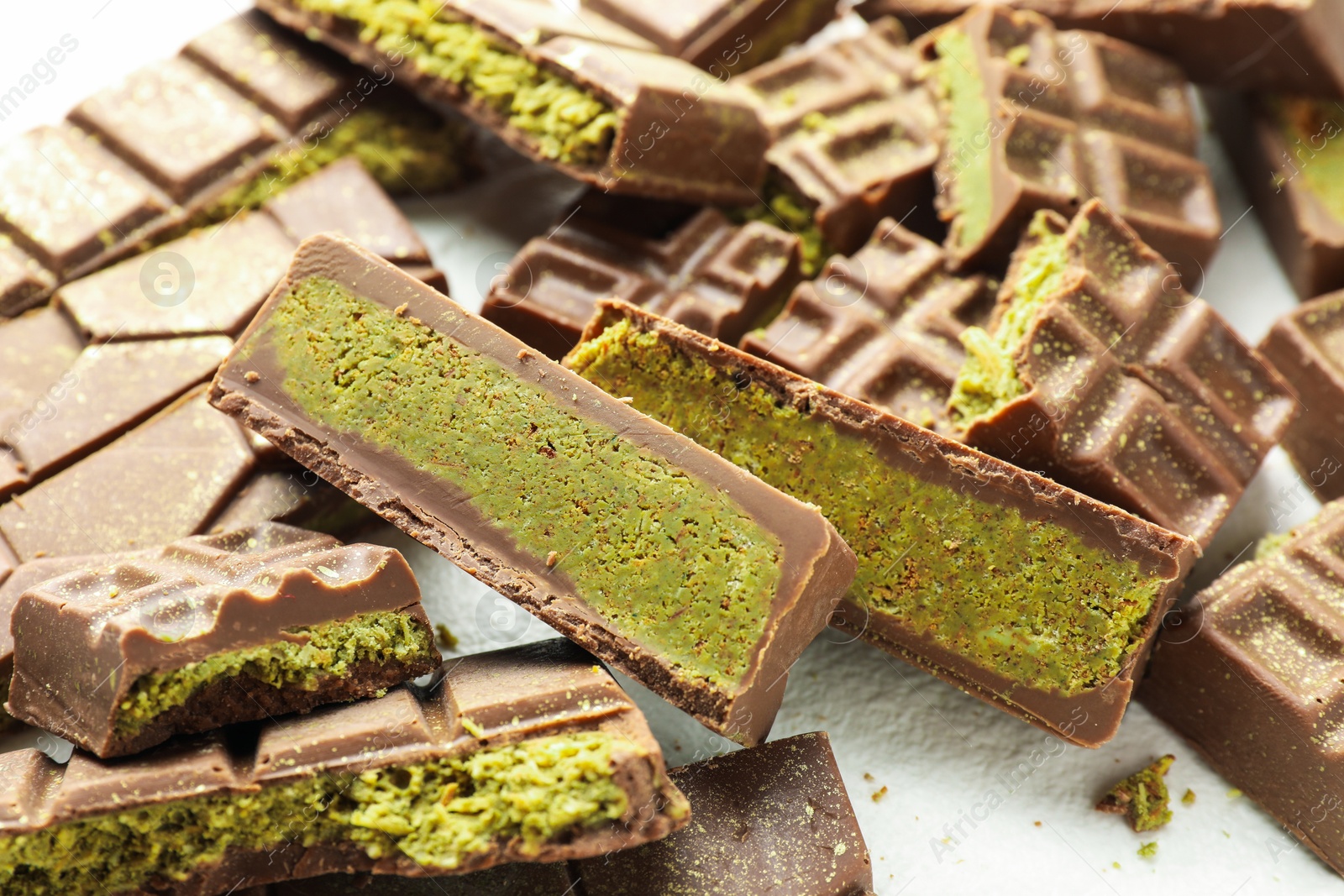 Pieces of tasty Dubai chocolate with pistachios and knafeh on white table, closeup Photo of Pieces of tasty Dubai chocolate with pistachios and knafeh on white table, closeup