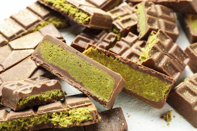 Photo of Pieces of tasty Dubai chocolate with pistachios and knafeh on white table, closeup