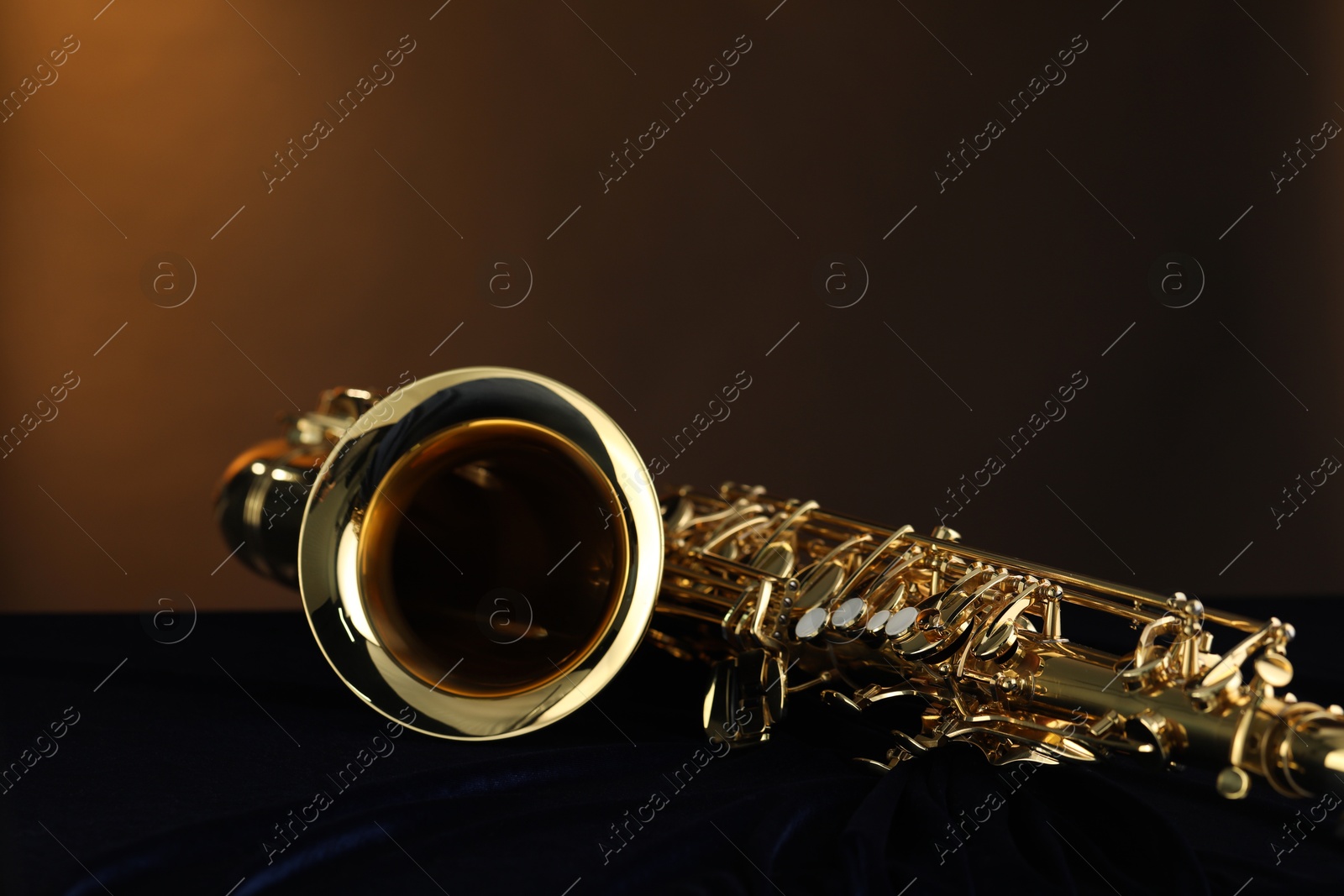 Photo of Jazz. One beautiful saxophone on dark blue fabric against brown background, closeup. Space for text