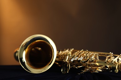 Photo of Jazz. One beautiful saxophone on dark blue fabric against brown background, closeup. Space for text