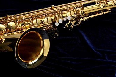 Photo of Jazz. One beautiful saxophone on dark blue fabric, closeup. Space for text