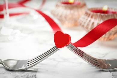 Romantic place setting for Valentine's day. Decorative heart between forks on white marble table, closeup