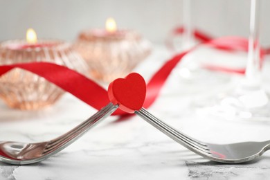 Photo of Romantic place setting for Valentine's day. Decorative heart between forks on white marble table, closeup