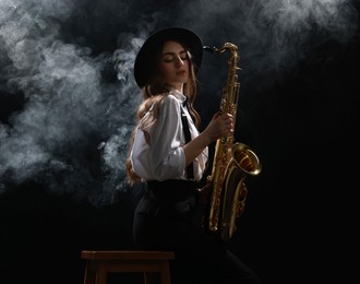 Photo of Professional musician playing saxophone on dark background with smoke