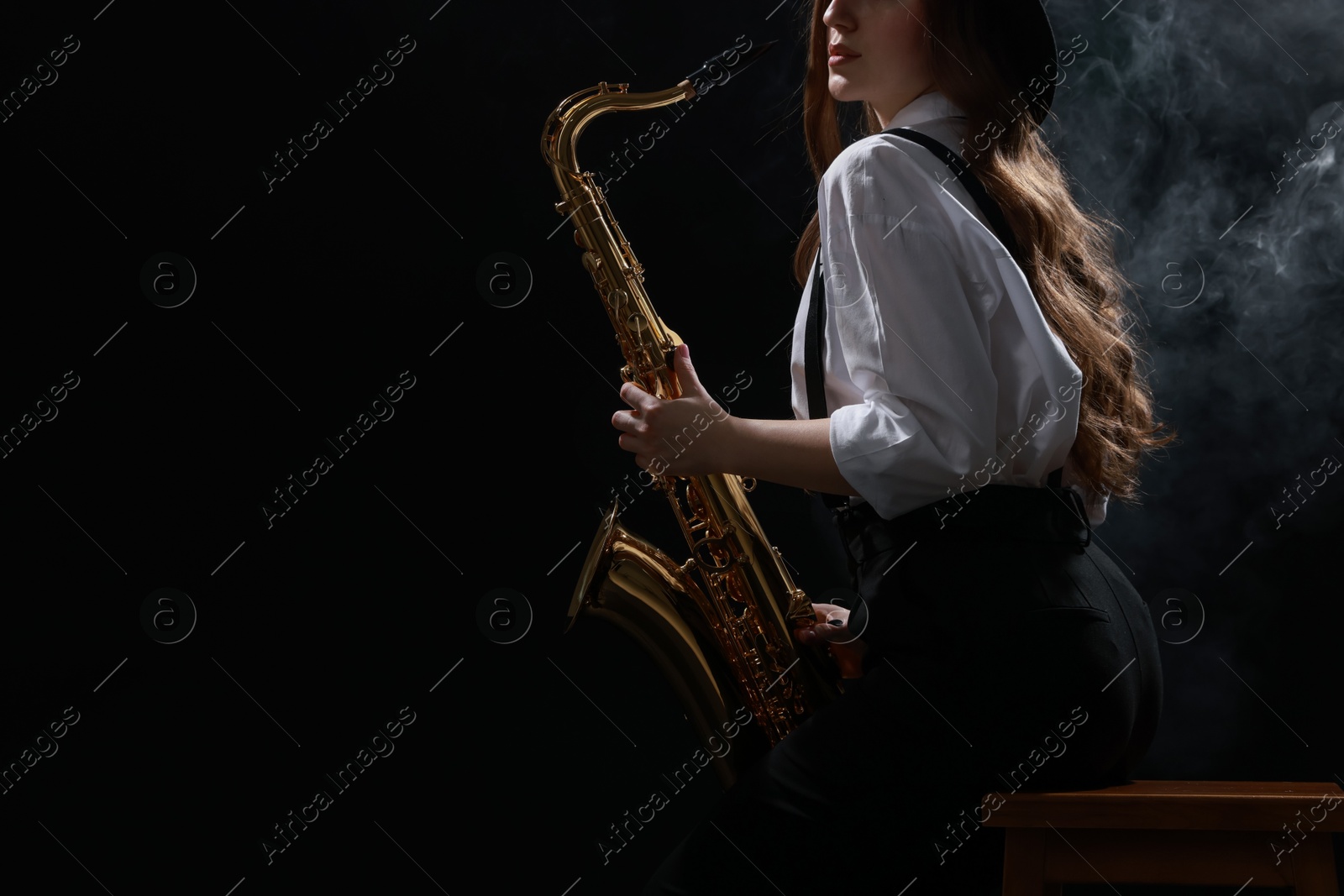 Photo of Professional musician playing saxophone on dark background with smoke, closeup. Space for text