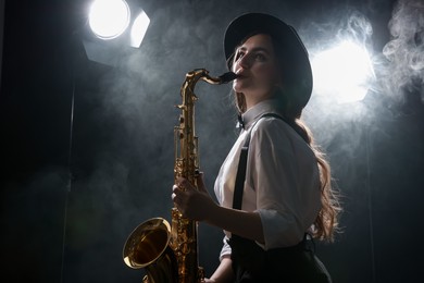 Photo of Professional musician playing saxophone on dark background with lights and smoke. Space for text