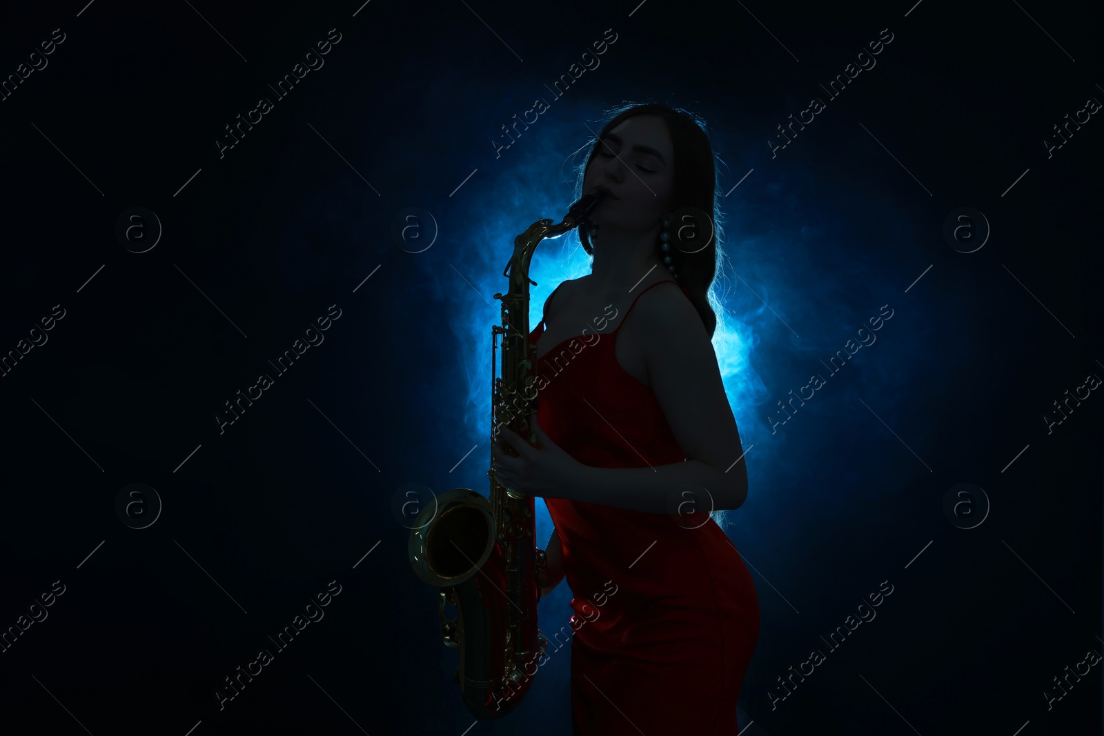 Photo of Professional musician playing saxophone on dark background with blue light and smoke