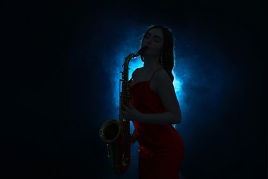 Photo of Professional musician playing saxophone on dark background with blue light and smoke