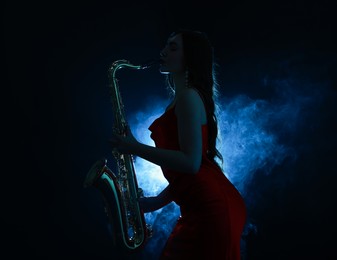 Photo of Professional musician playing saxophone on dark background with blue light and smoke