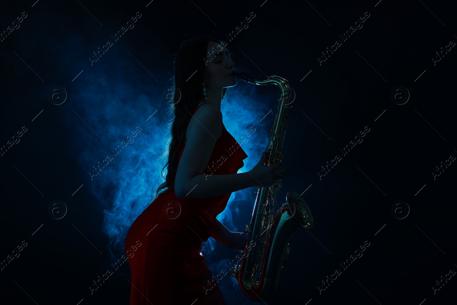 Photo of Professional musician playing saxophone on dark background with blue light and smoke