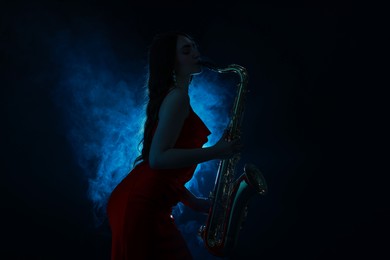 Photo of Professional musician playing saxophone on dark background with blue light and smoke