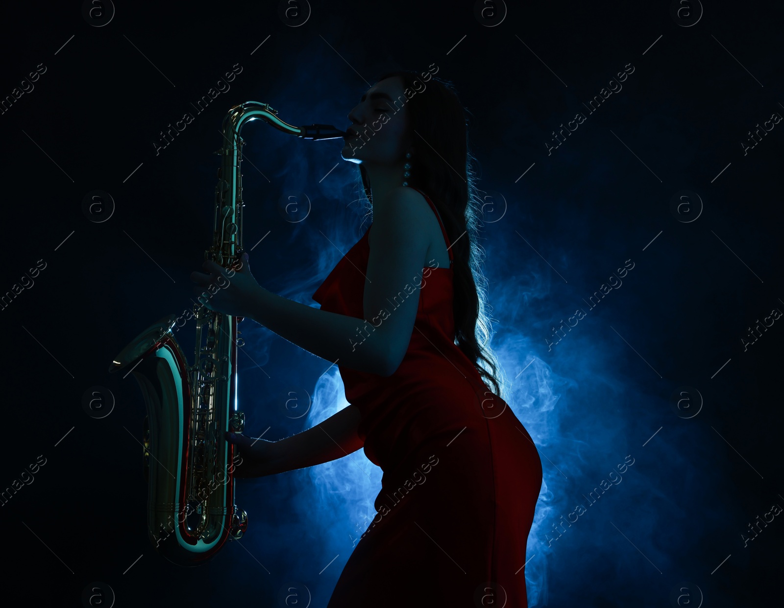 Photo of Professional musician playing saxophone on dark background with blue light and smoke