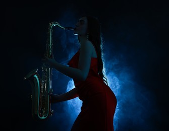 Photo of Professional musician playing saxophone on dark background with blue light and smoke