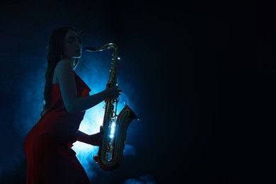 Professional musician playing saxophone on dark background with blue light and smoke. Space for text