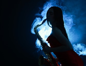 Photo of Professional musician playing saxophone on dark background with blue light and smoke. Space for text