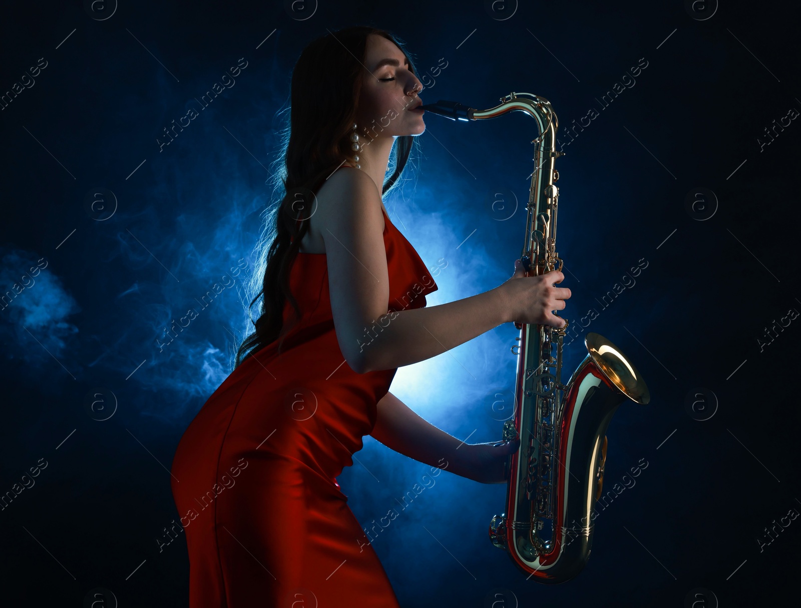 Photo of Professional musician playing saxophone on dark background with blue light and smoke