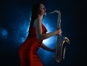 Photo of Professional musician playing saxophone on dark background with blue light and smoke