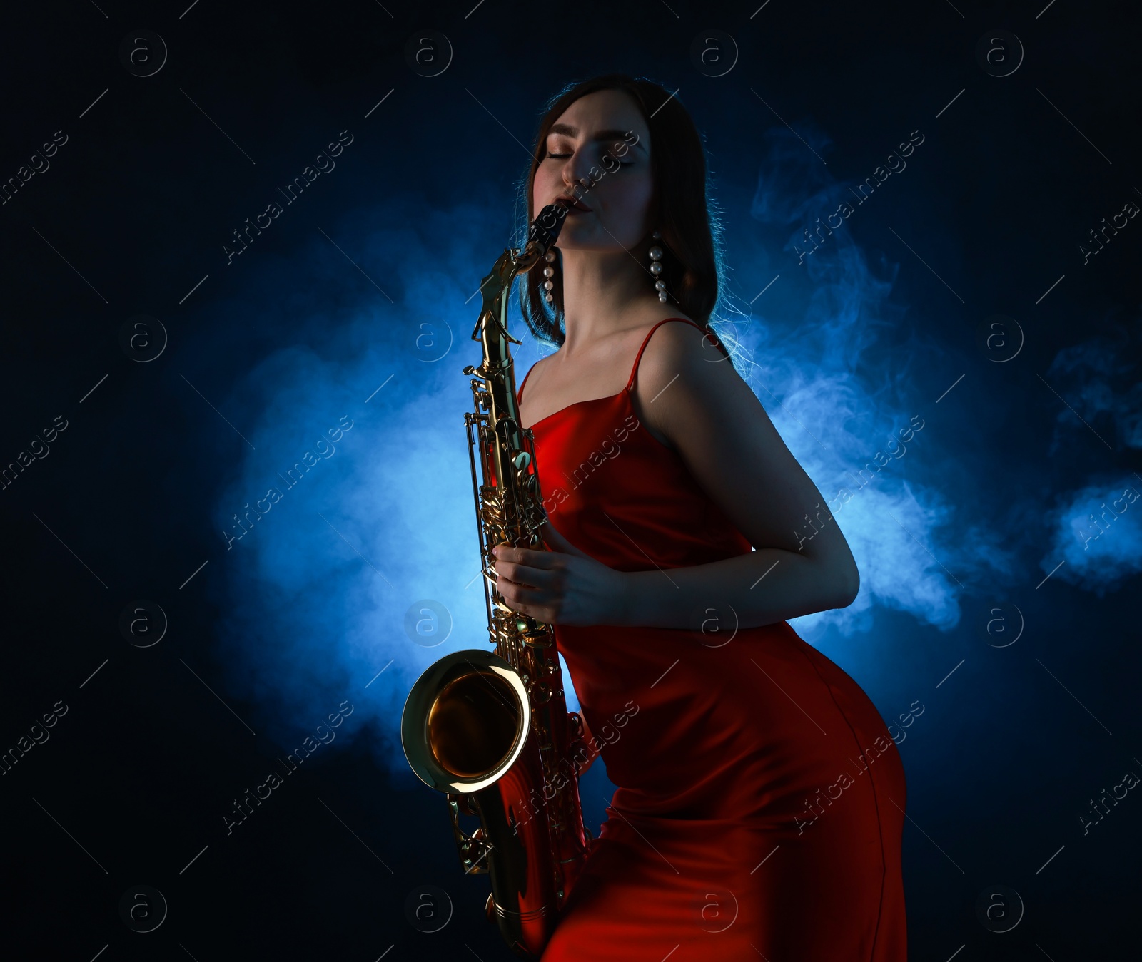 Photo of Professional musician playing saxophone on dark background with blue light and smoke