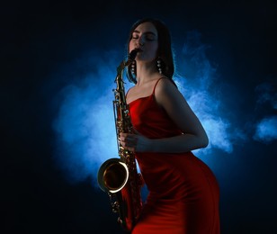 Photo of Professional musician playing saxophone on dark background with blue light and smoke