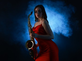 Photo of Professional musician playing saxophone on dark background with blue light and smoke. Space for text