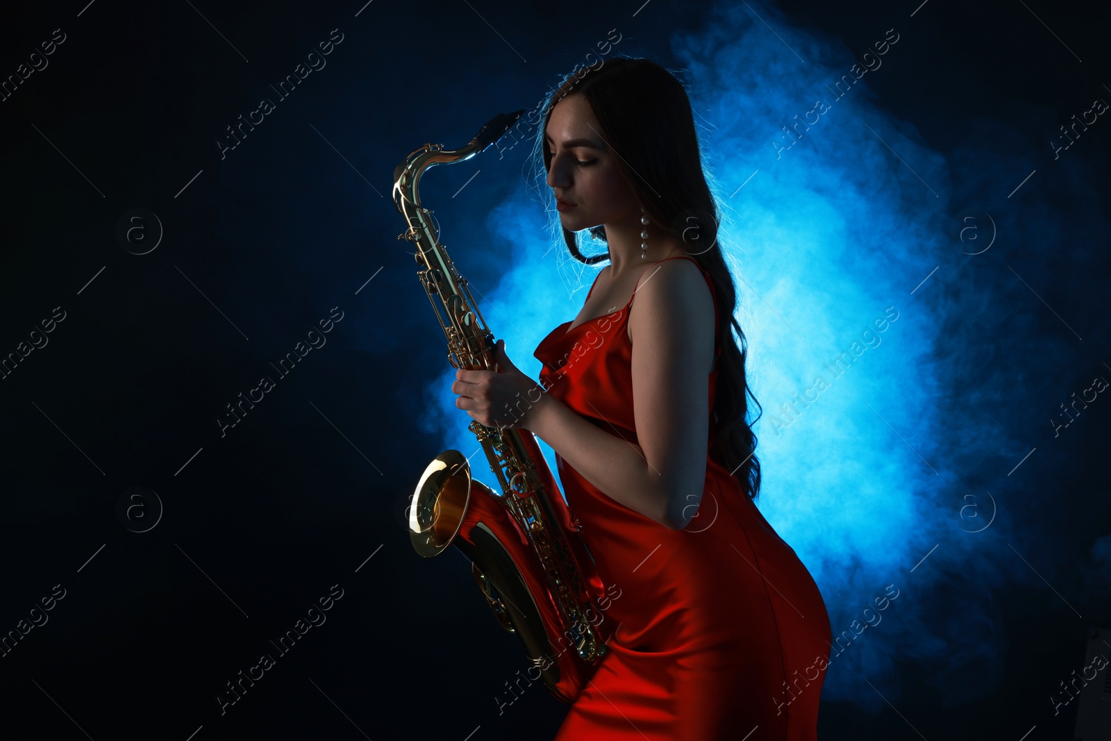 Photo of Professional musician playing saxophone on dark background with blue light and smoke. Space for text