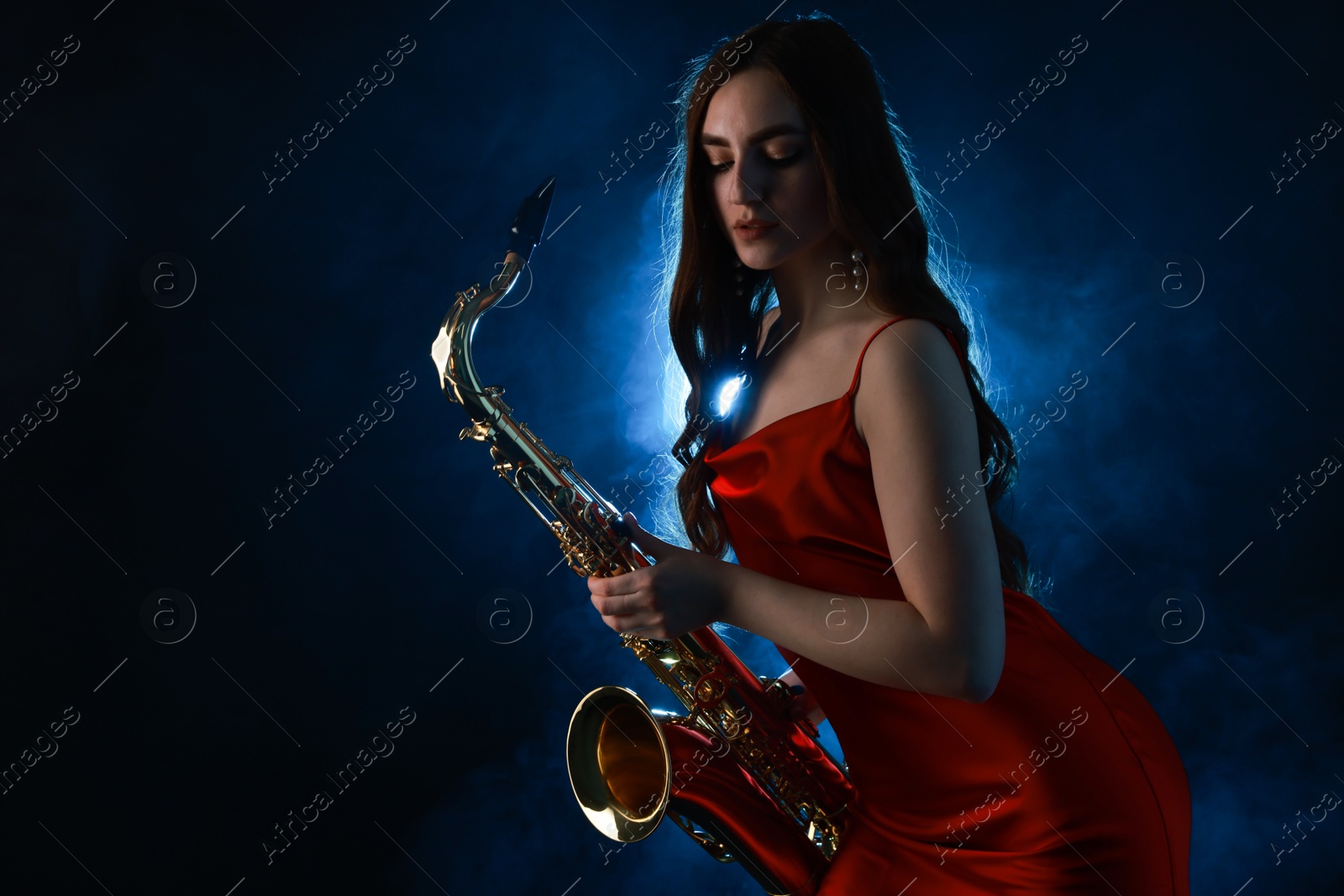 Photo of Professional musician playing saxophone on dark background with blue light and smoke