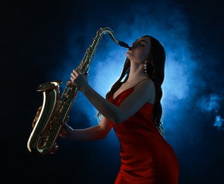 Photo of Professional musician playing saxophone on dark background with blue light and smoke