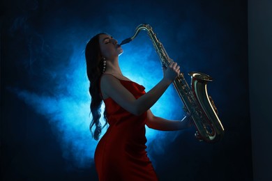 Photo of Professional musician playing saxophone on dark background with blue light and smoke