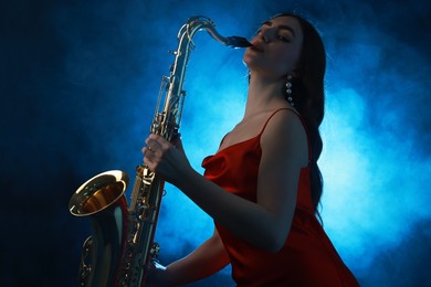 Professional musician playing saxophone on dark background with blue light and smoke