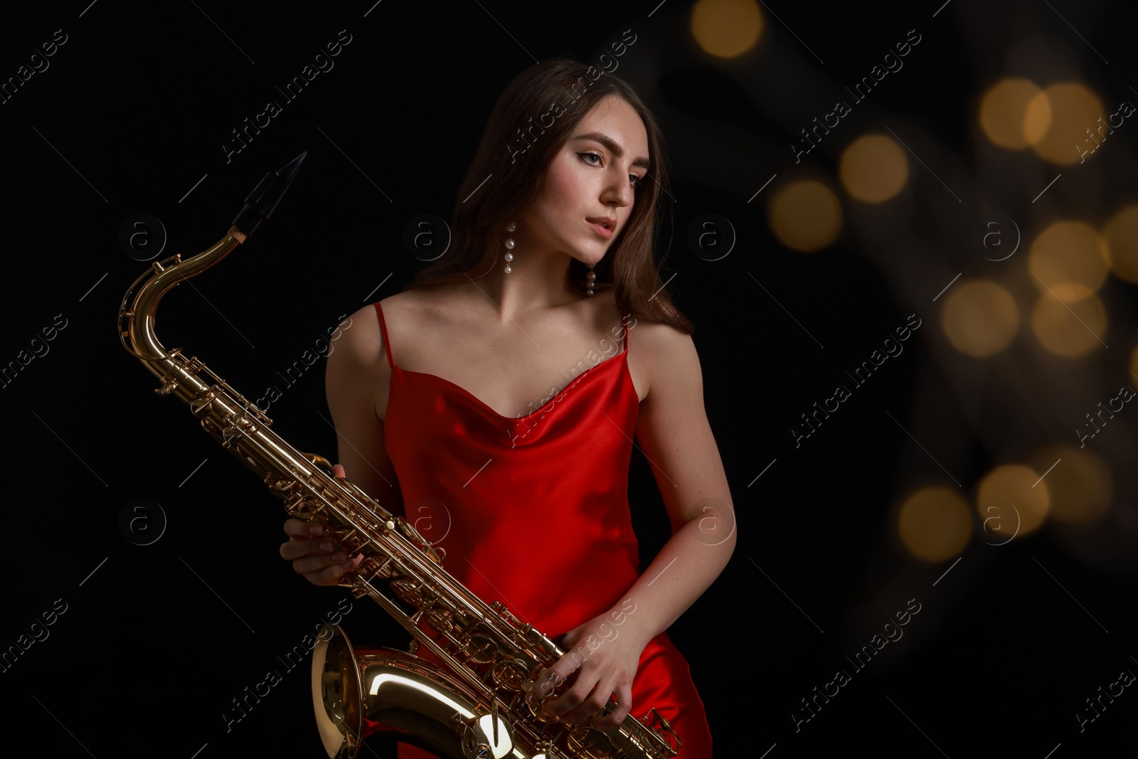 Photo of Professional musician playing saxophone on black background with blurred lights. Bokeh effect