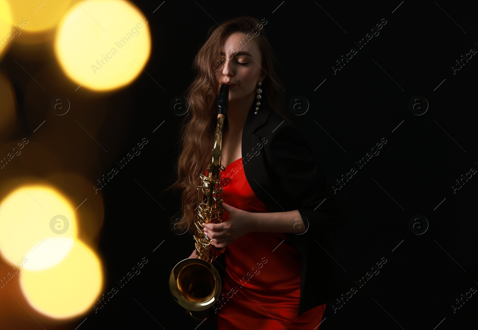 Photo of Professional musician playing saxophone on black background with blurred lights. Bokeh effect