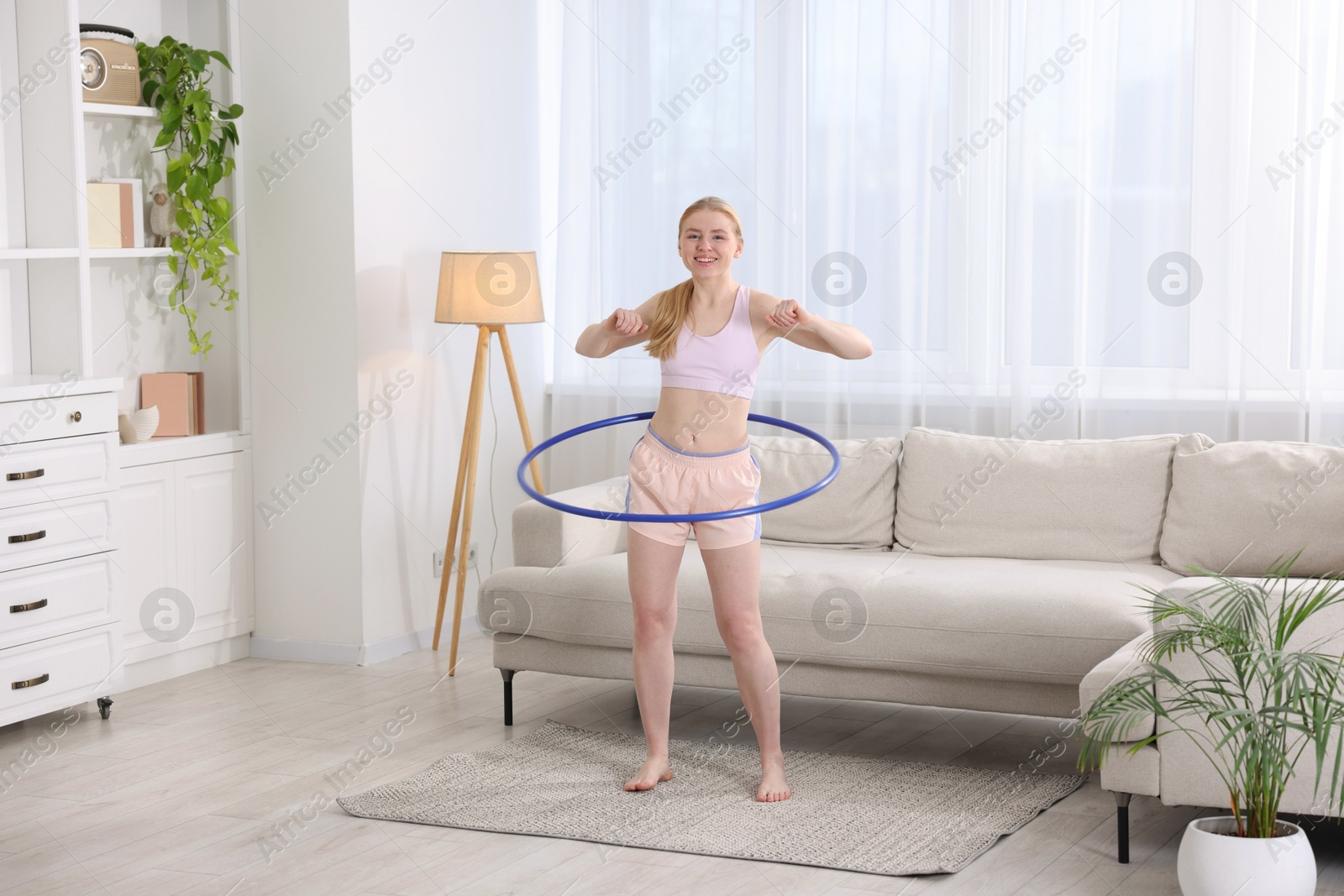 Photo of Beautiful young woman exercising with hula hoop at home