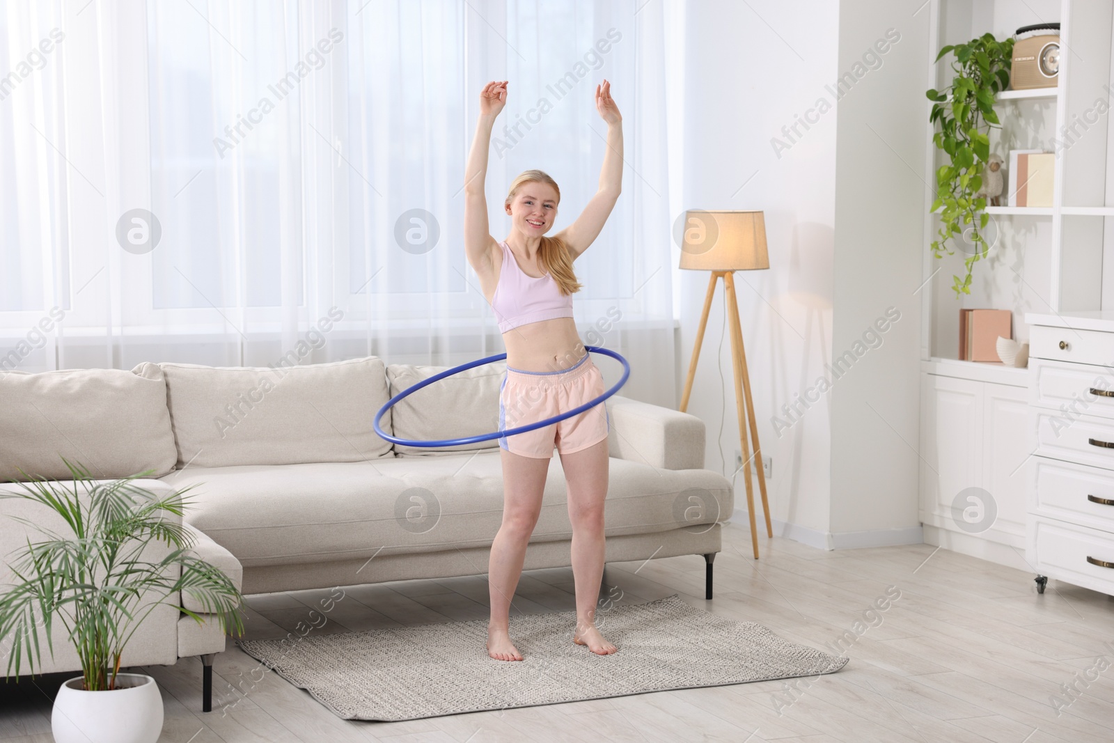 Photo of Beautiful young woman exercising with hula hoop at home