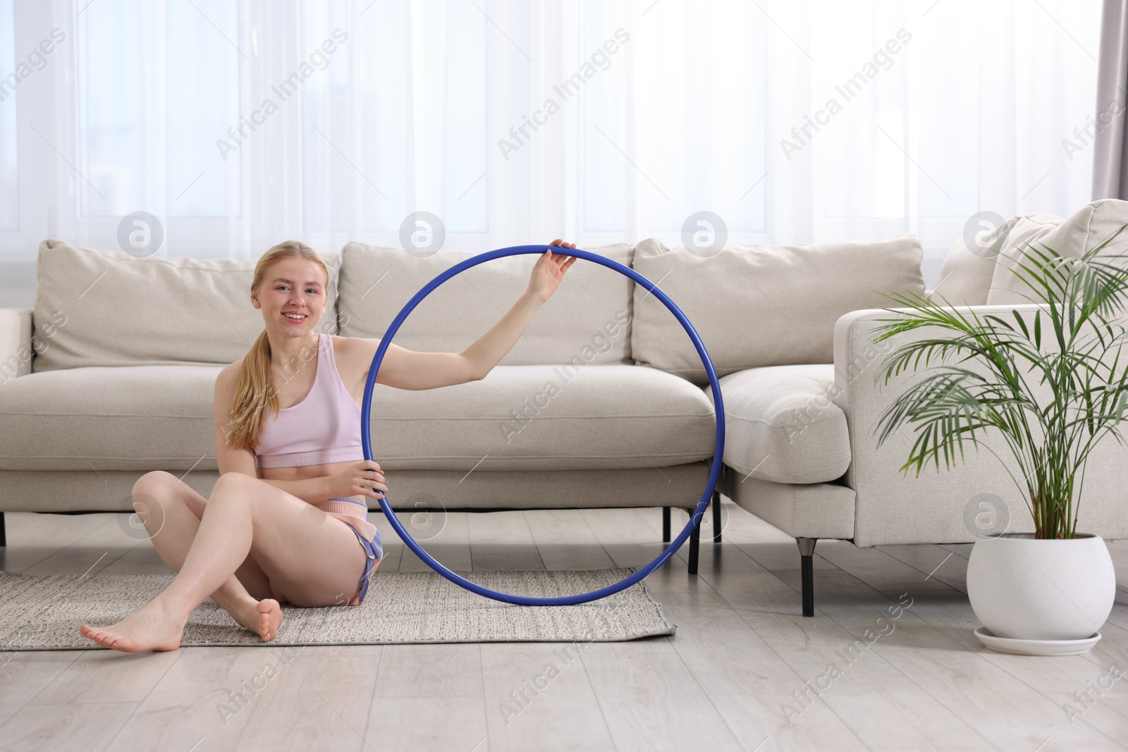 Photo of Beautiful young woman with hula hoop on floor at home