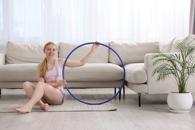 Photo of Beautiful young woman with hula hoop on floor at home