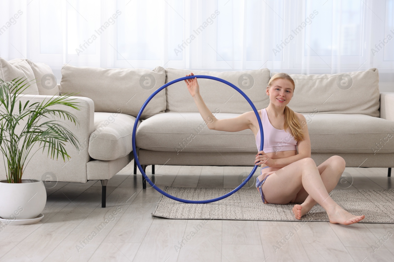 Photo of Beautiful young woman with hula hoop on floor at home