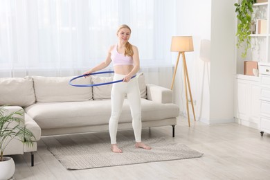 Beautiful young woman exercising with hula hoop at home