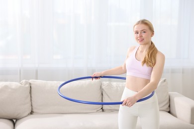 Photo of Beautiful young woman exercising with hula hoop at home