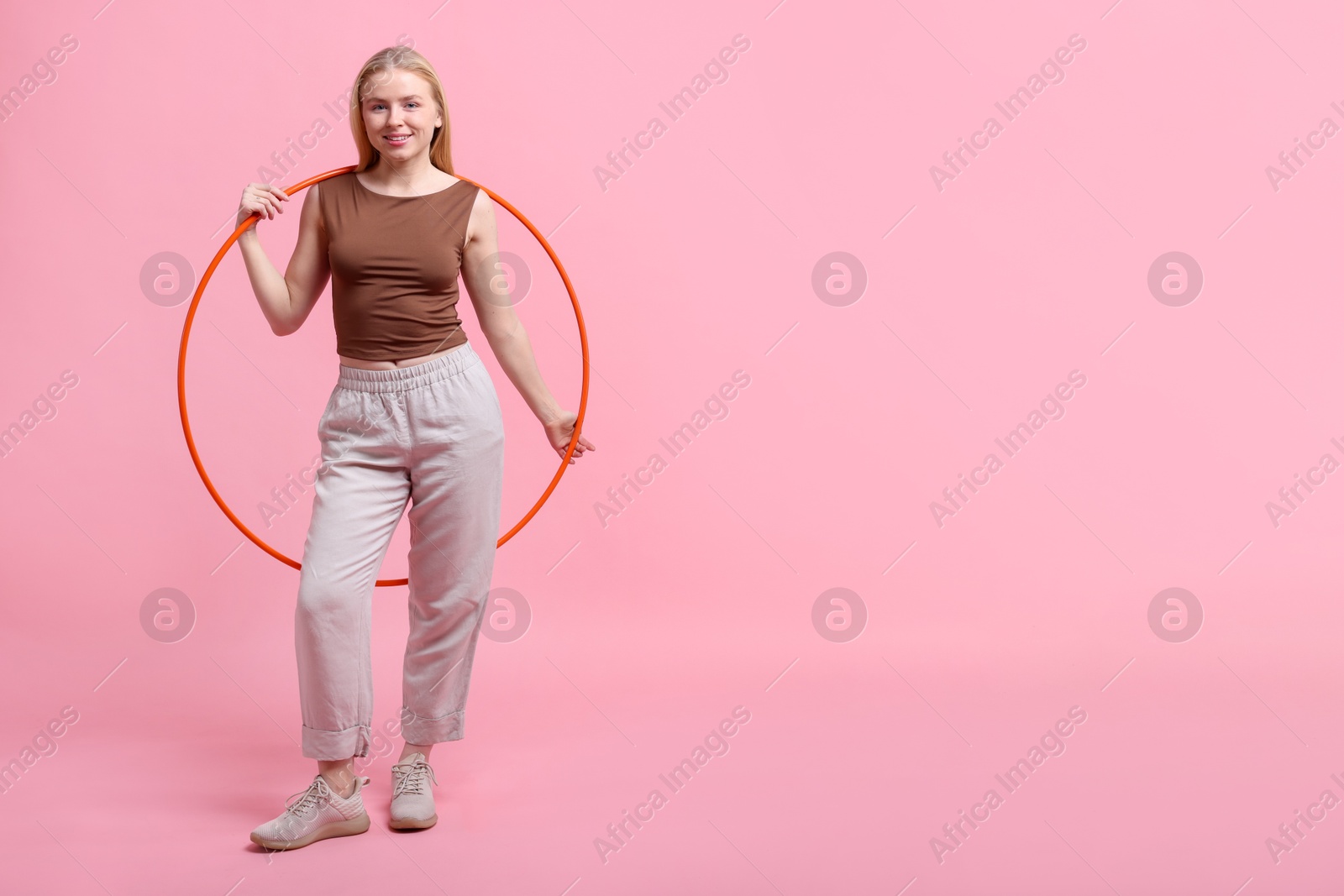 Photo of Beautiful young woman with hula hoop on pink background, space for text