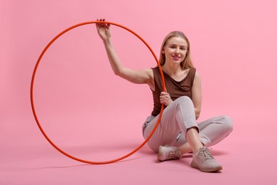 Beautiful young woman with hula hoop on pink background